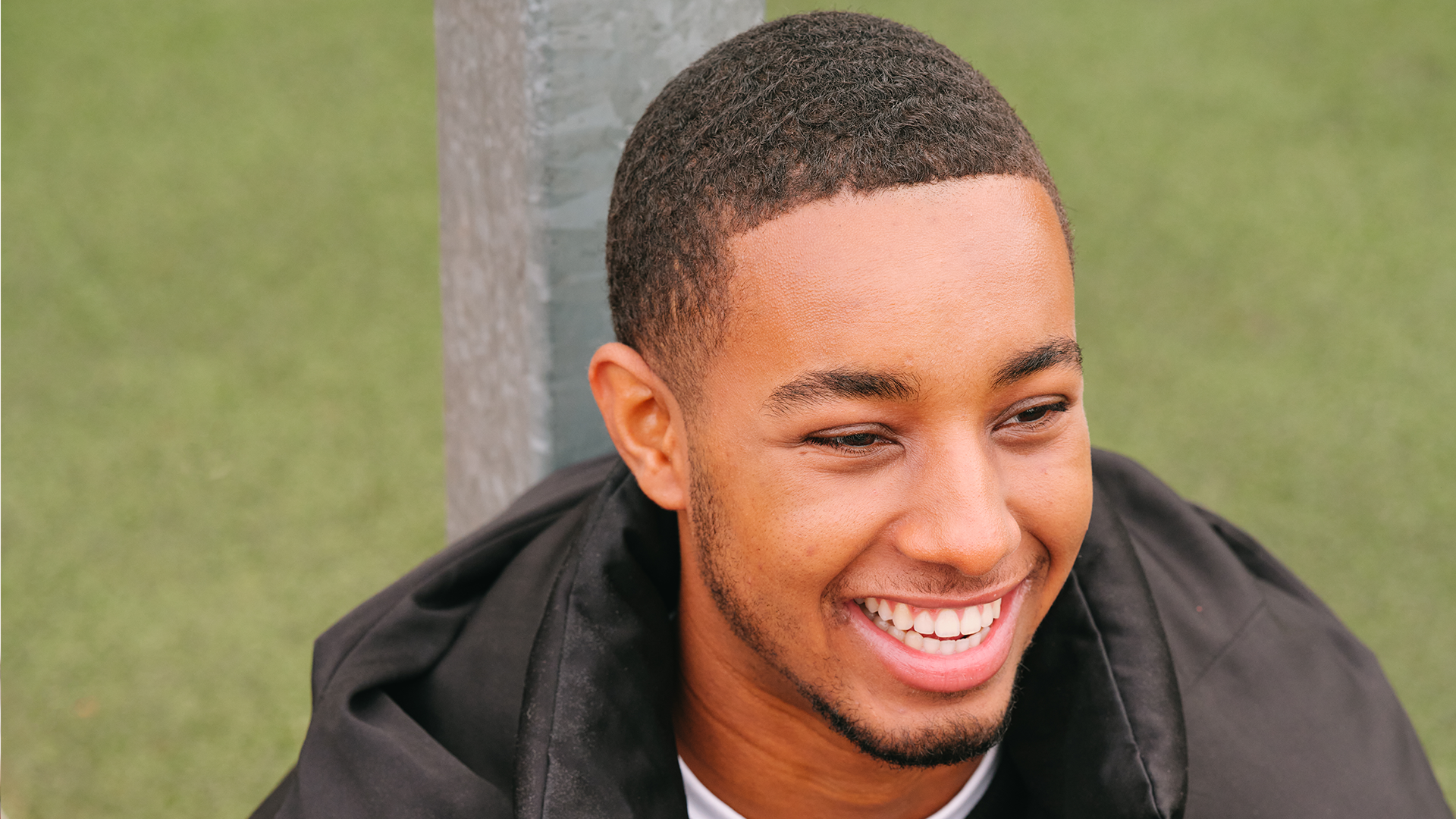 A young Black man smiling in the park.