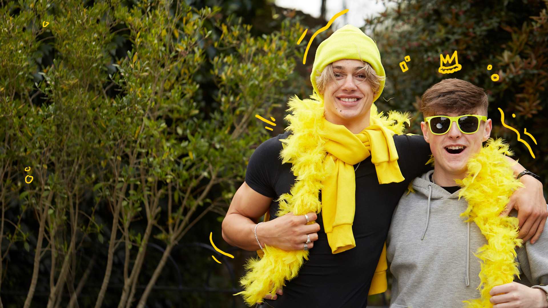 Two young people with their arms around each other. They are wearing a yellow feather boa, yellow hat and yellow sunglasses.