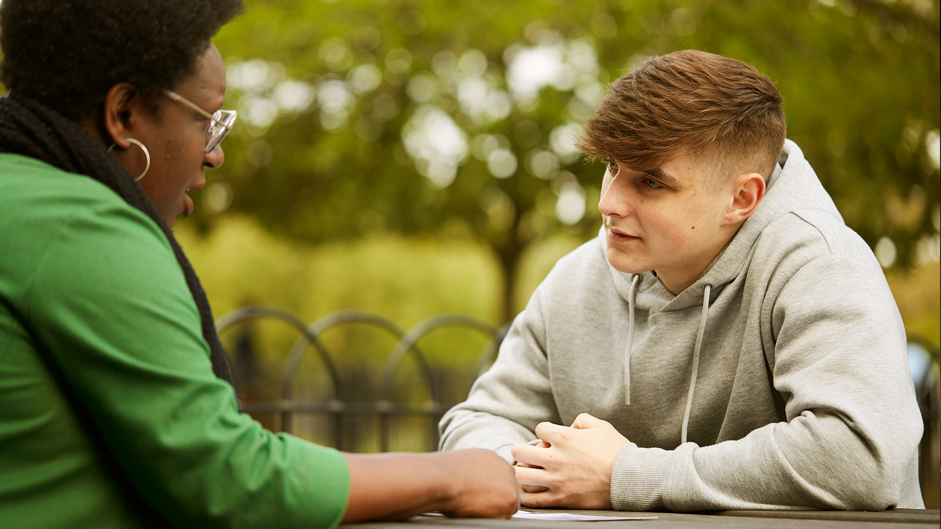 A young person talking to a trusted adult outside on a bench.