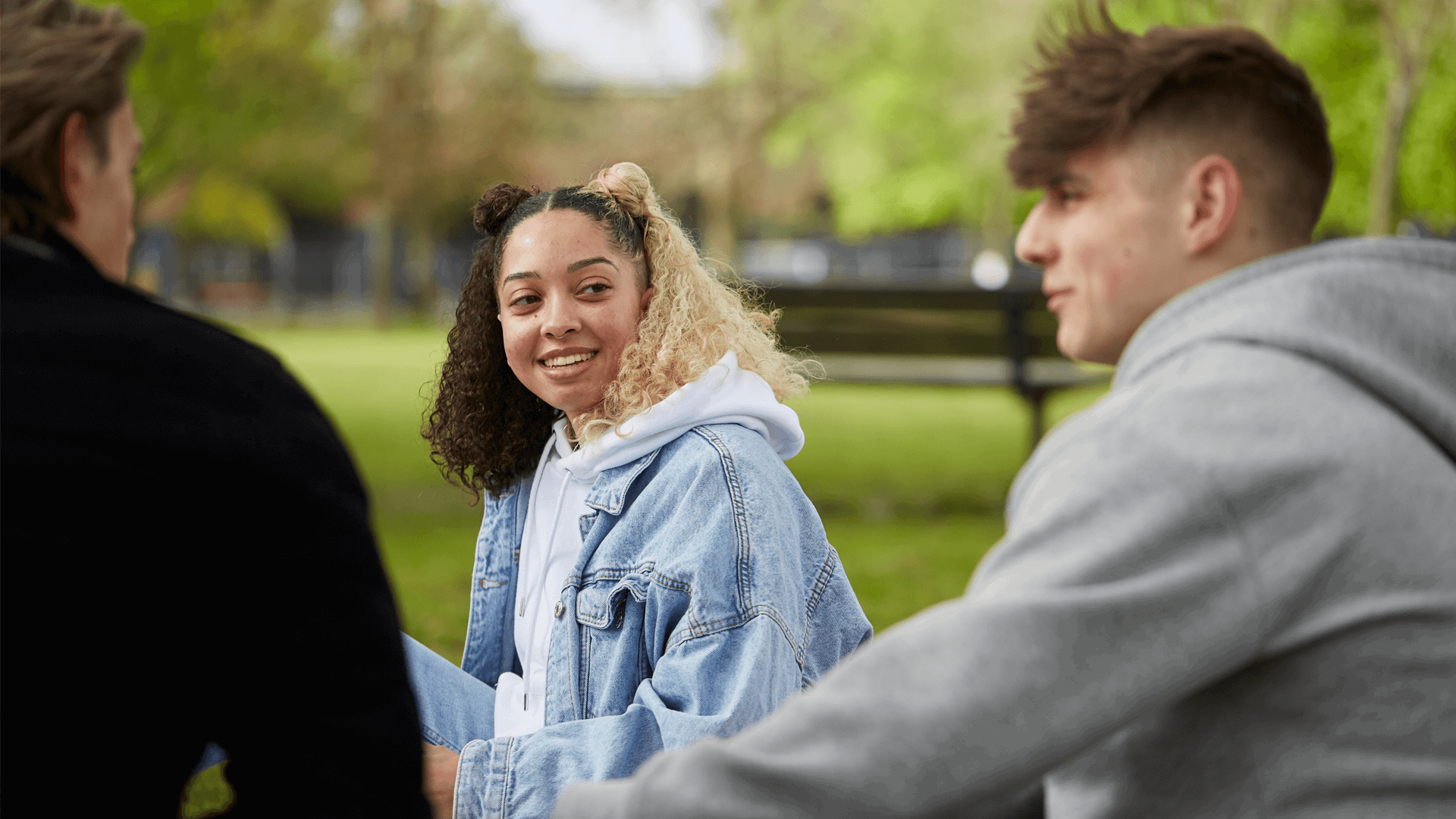 medium-shot-of-a-girl-smiling-to-her-two-other-boyfriens-while-sitting-on-the-ground-in-the-park