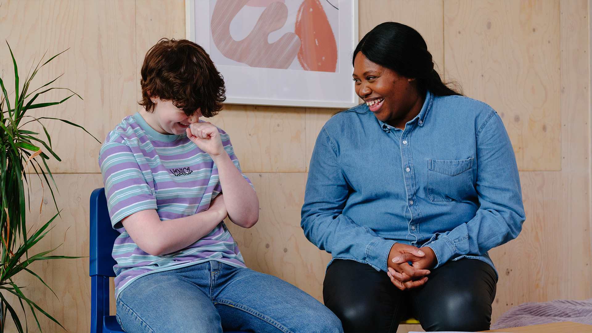 A white non-binary teenager laughing with an older Black woman in a professional setting.