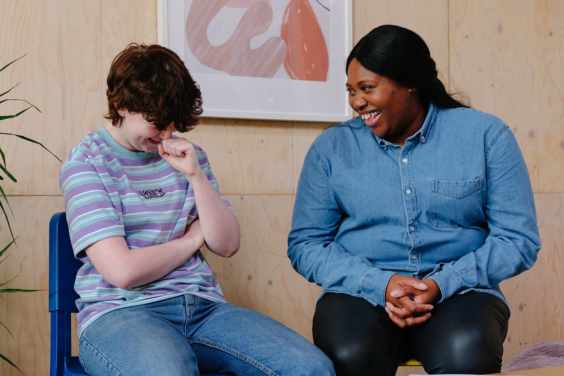 A white non-binary teenager laughing with an older Black woman in a professional setting.