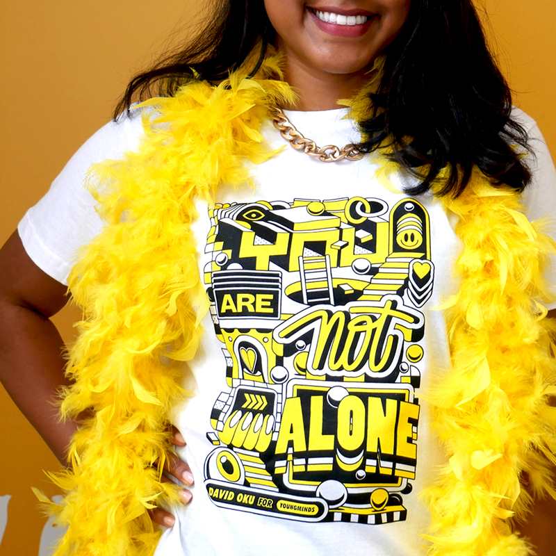 A close up of a woman smiling wearing a yellow feather bower, gold chain and our David Oku's bespoke 'You are not alone' graphic #HelloYellow T-shirt.