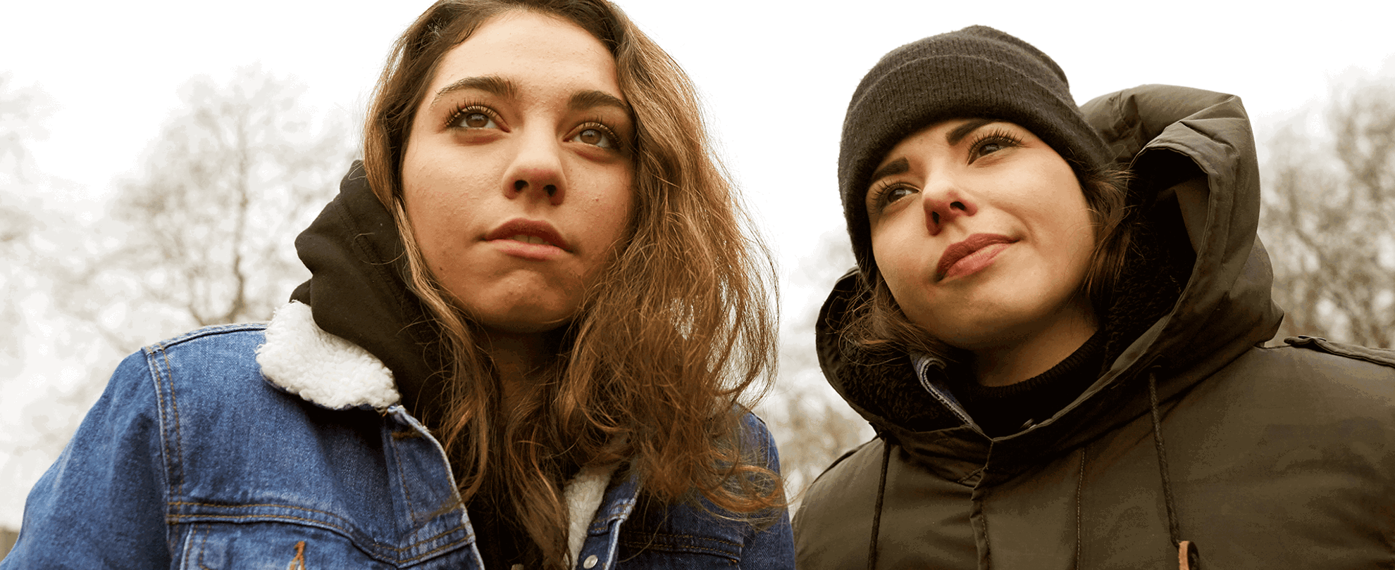 Two young people standing together and looking up at something.