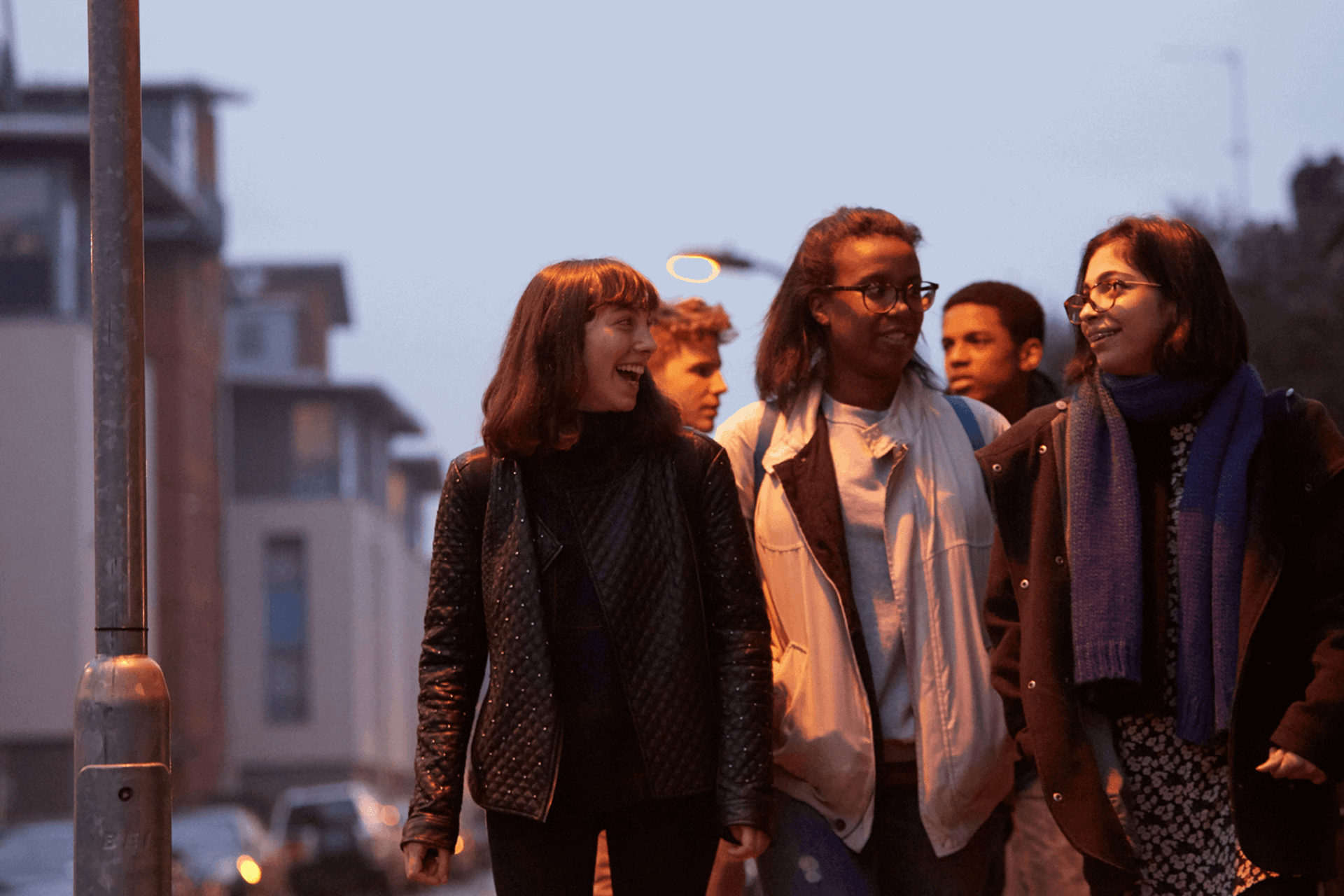 wide-shot-of-a-group-of-young-people-smiling-while-walking-on-a-street-with-houses-at-night