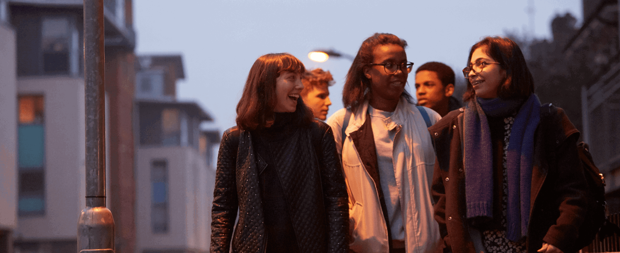 wide-shot-of-a-group-of-young-people-smiling-while-walking-on-a-street-with-houses-at-night