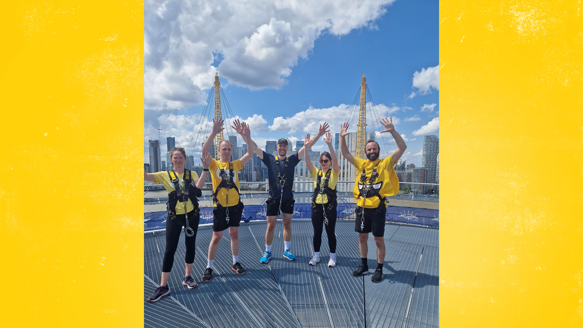 Five YoungMinds staff members at the top of The O2 wearing yellow t-shirts. Their hands are all raised in the air.
