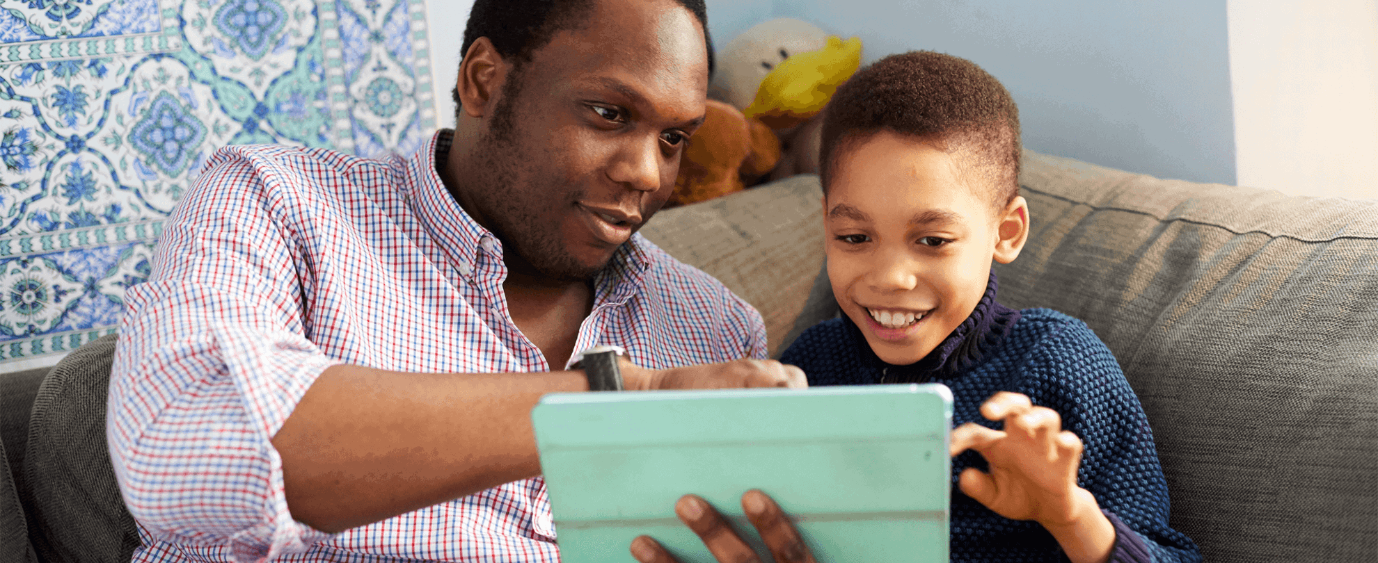 A father and son using a tablet together on the sofa smiling