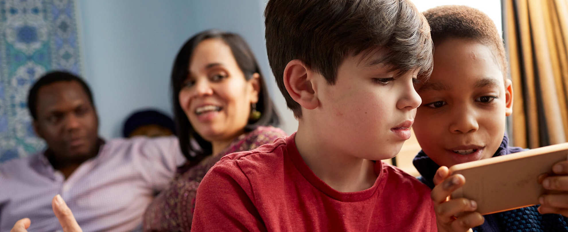 A family relaxing at home with parents chatting and children playing on a tablet