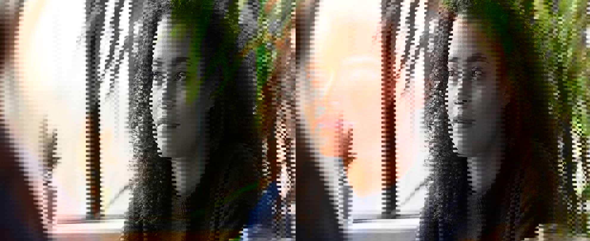 A girl with curly hair sitting in a cafe. She is looking away and smiling beside a window.