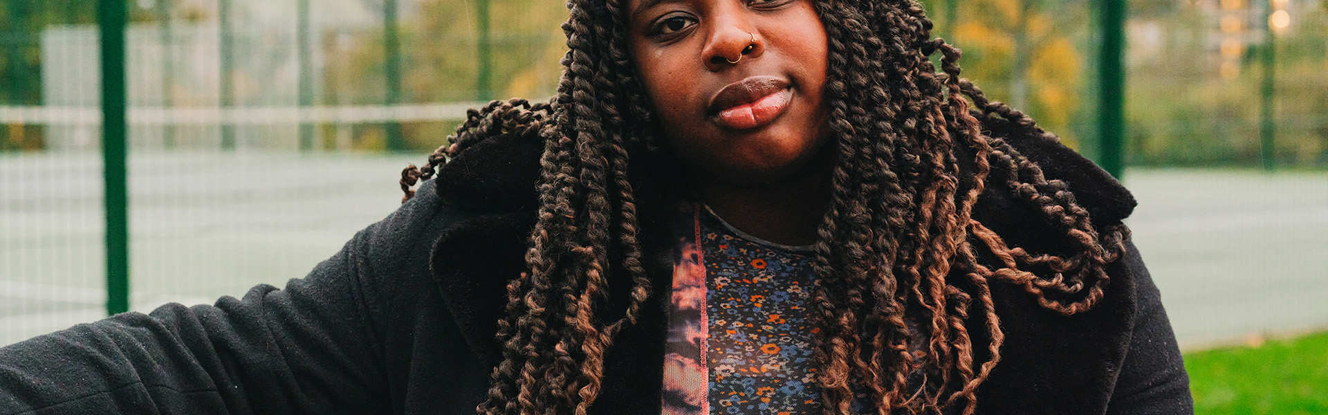 A young Black woman sitting on a bench in the park.
