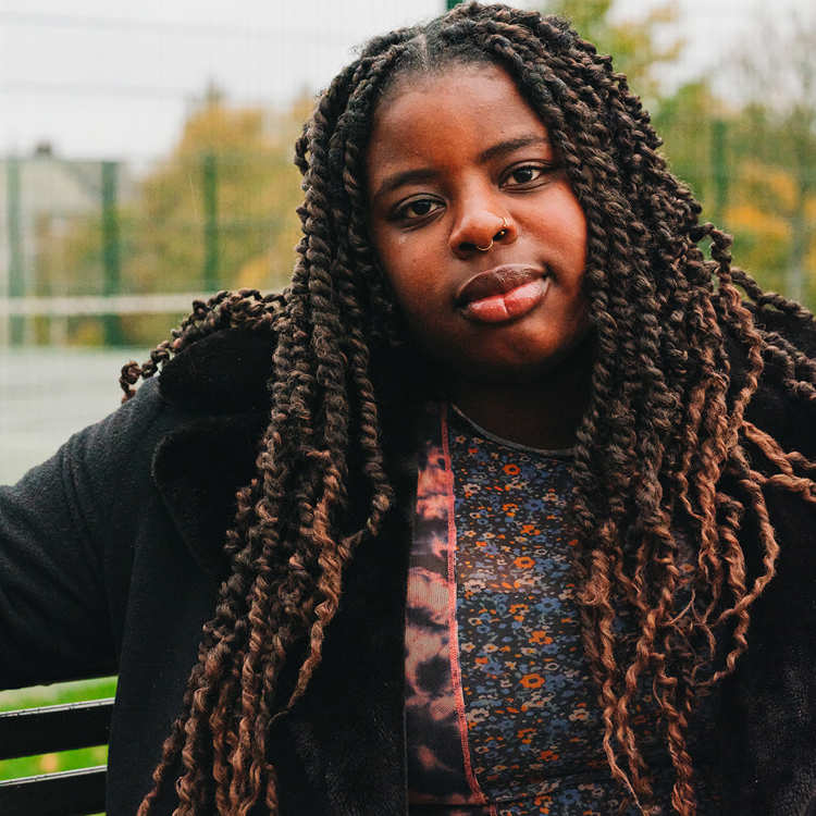 A young Black woman sitting on a bench in the park.