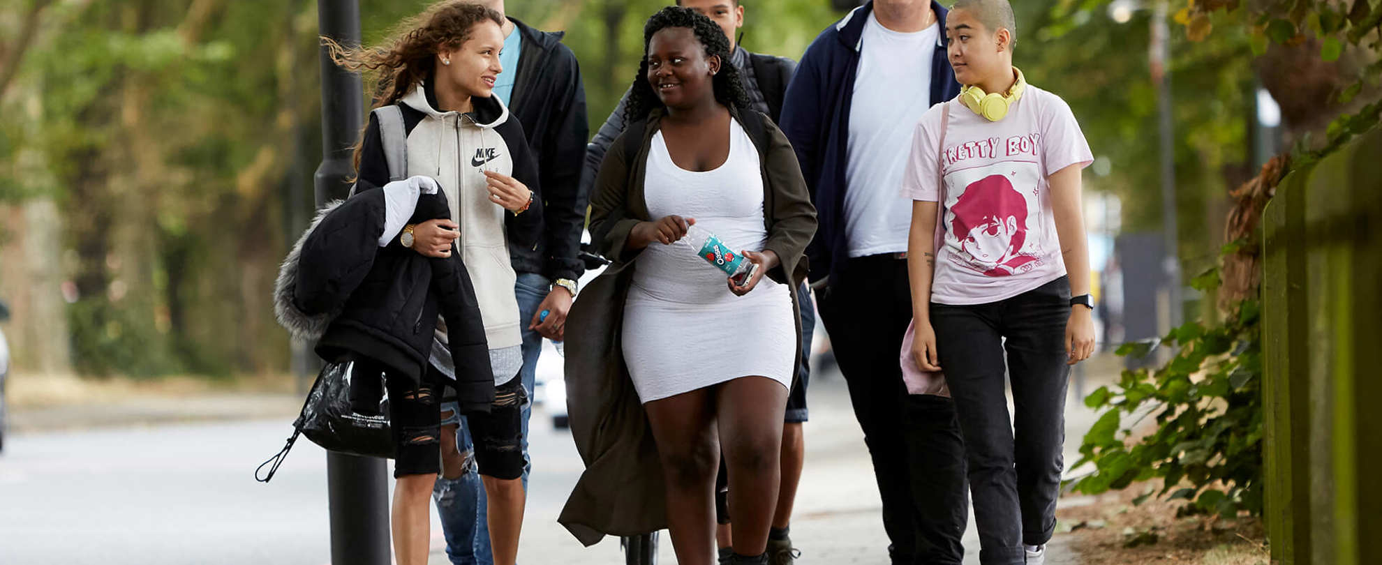 Six young people chatting as they walk through a park together.