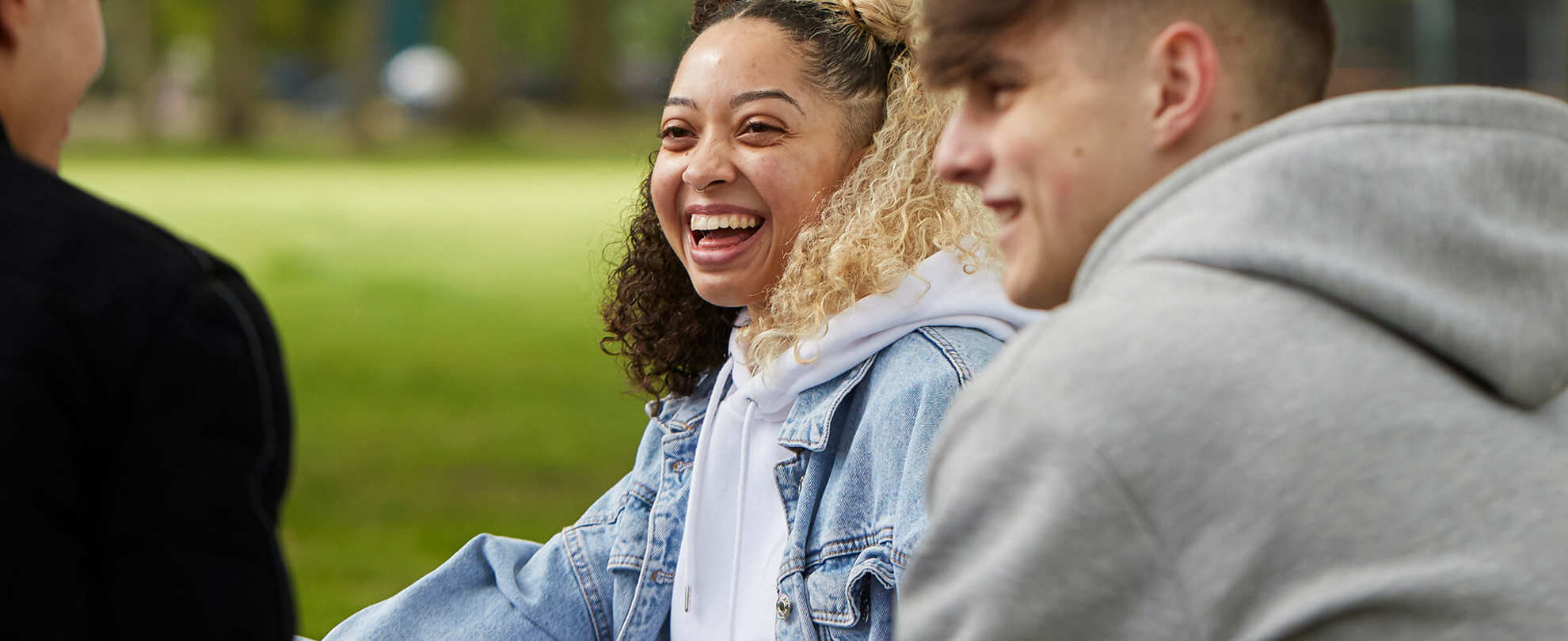 Three young people sitting in a park, laughing and chatting.