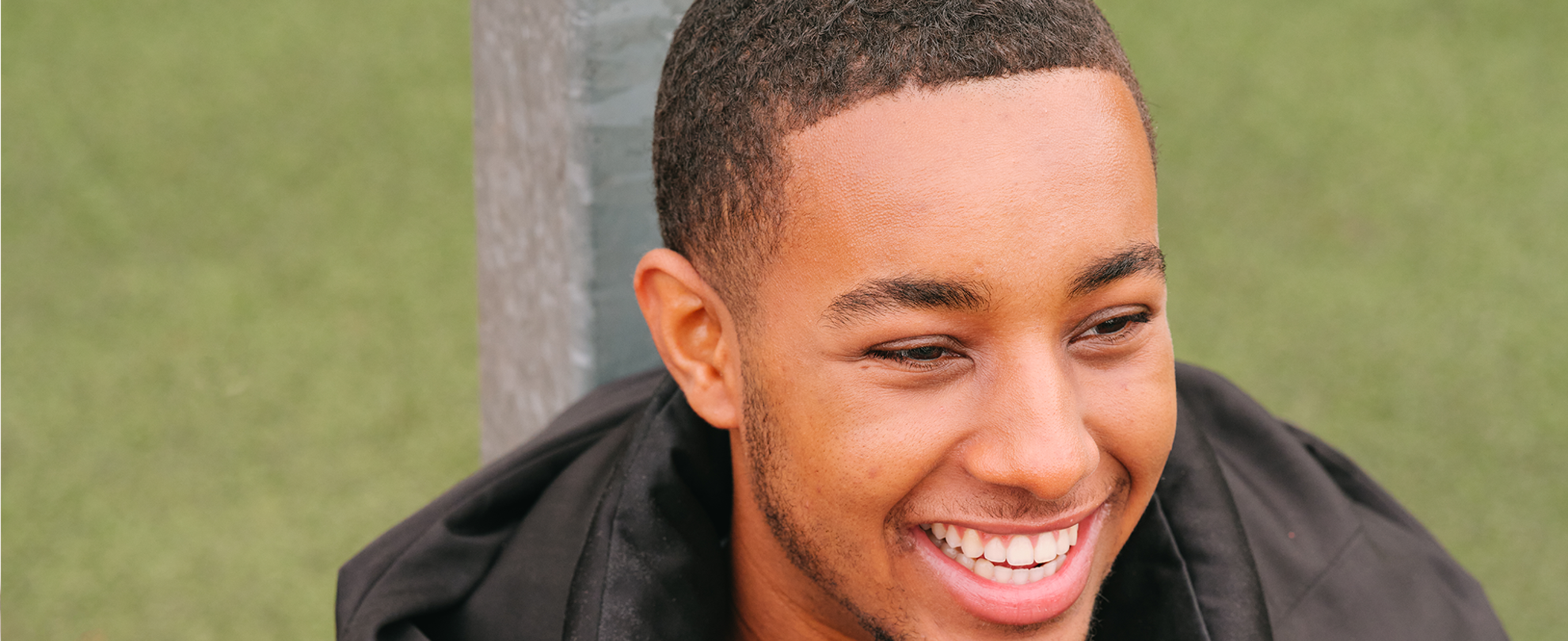 A young Black man smiling in the park.