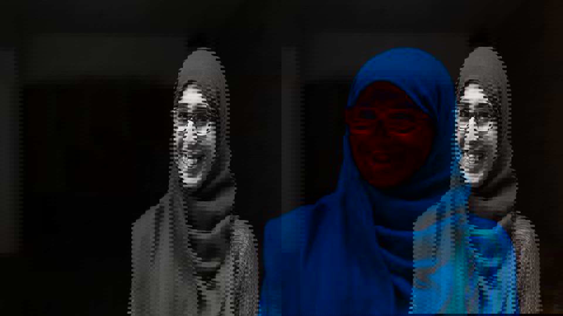 A young woman smiling and wearing a blue hijab and glasses.
