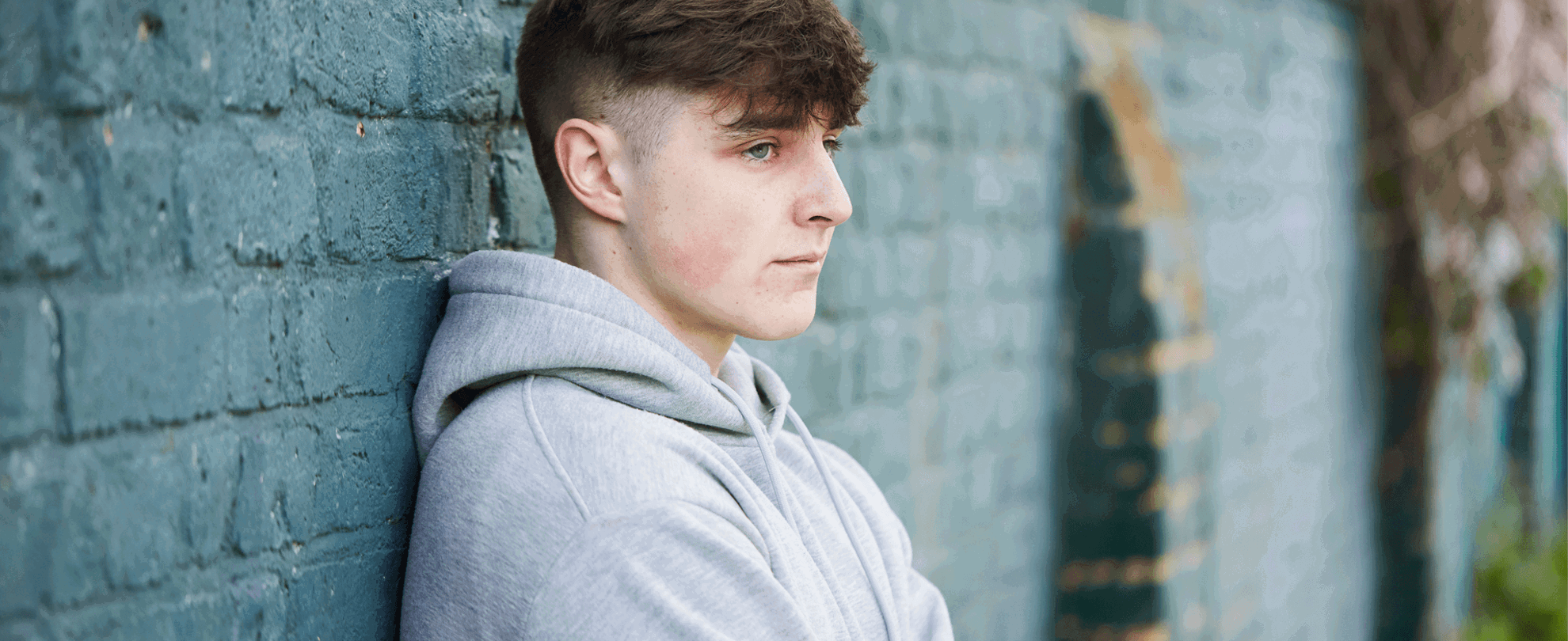 A young person standing with their back against a brick wall.