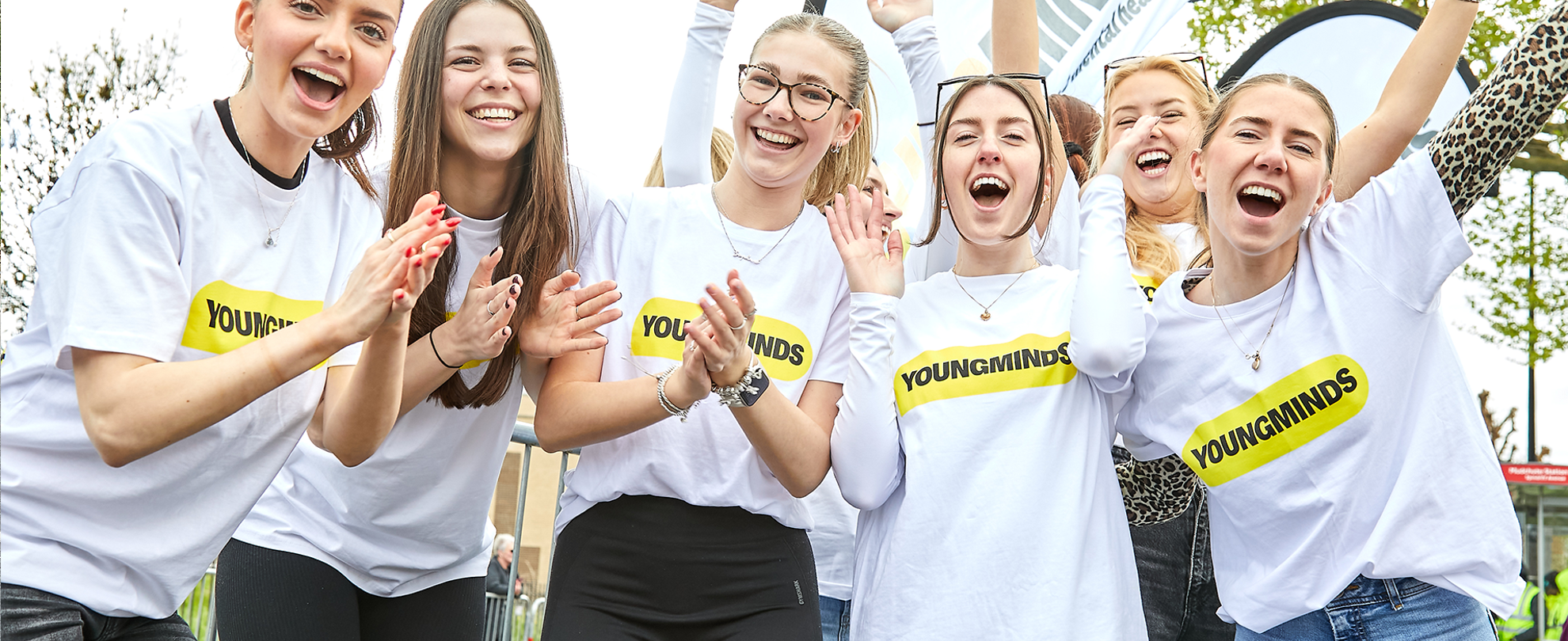 The YoungMinds fundraising team cheering with their hands in the air at the marathon. They are wearing YoungMinds t-shirts and have YoungMinds banners.