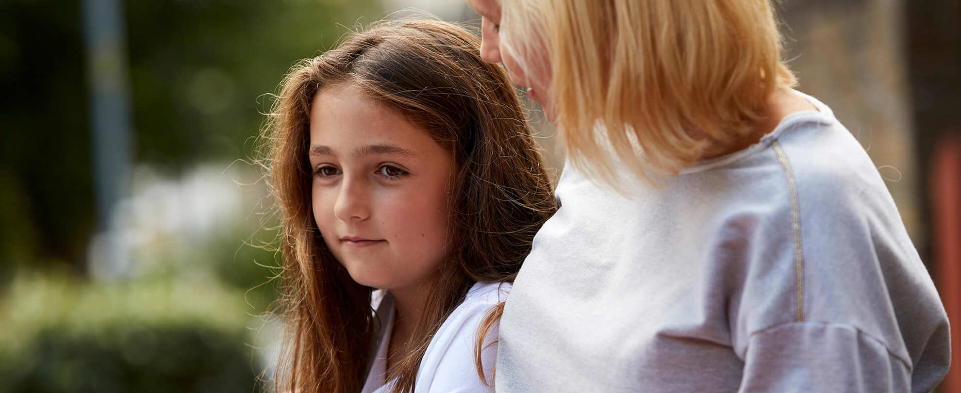 A mother comforts her sad looking daughter outdoors
