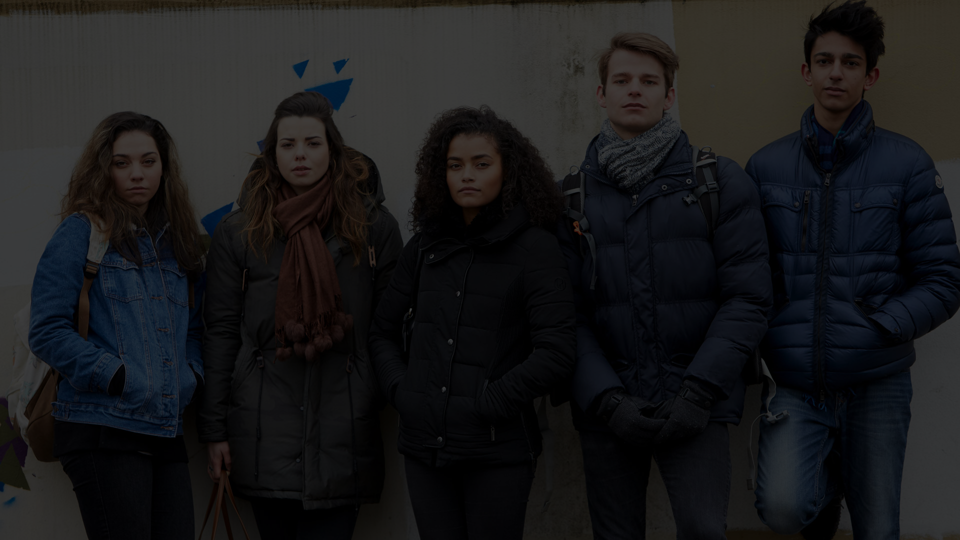 A line of young people standing against a wall outside.