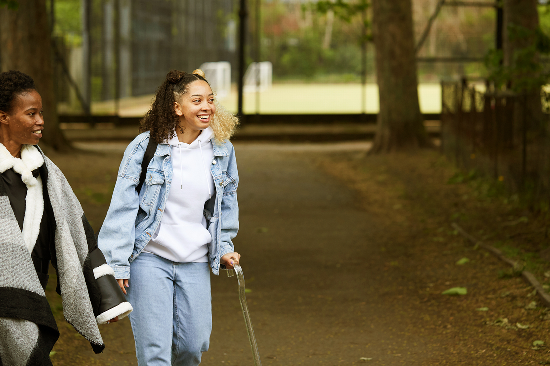 A girl with a crutch and an adult walking in the park.