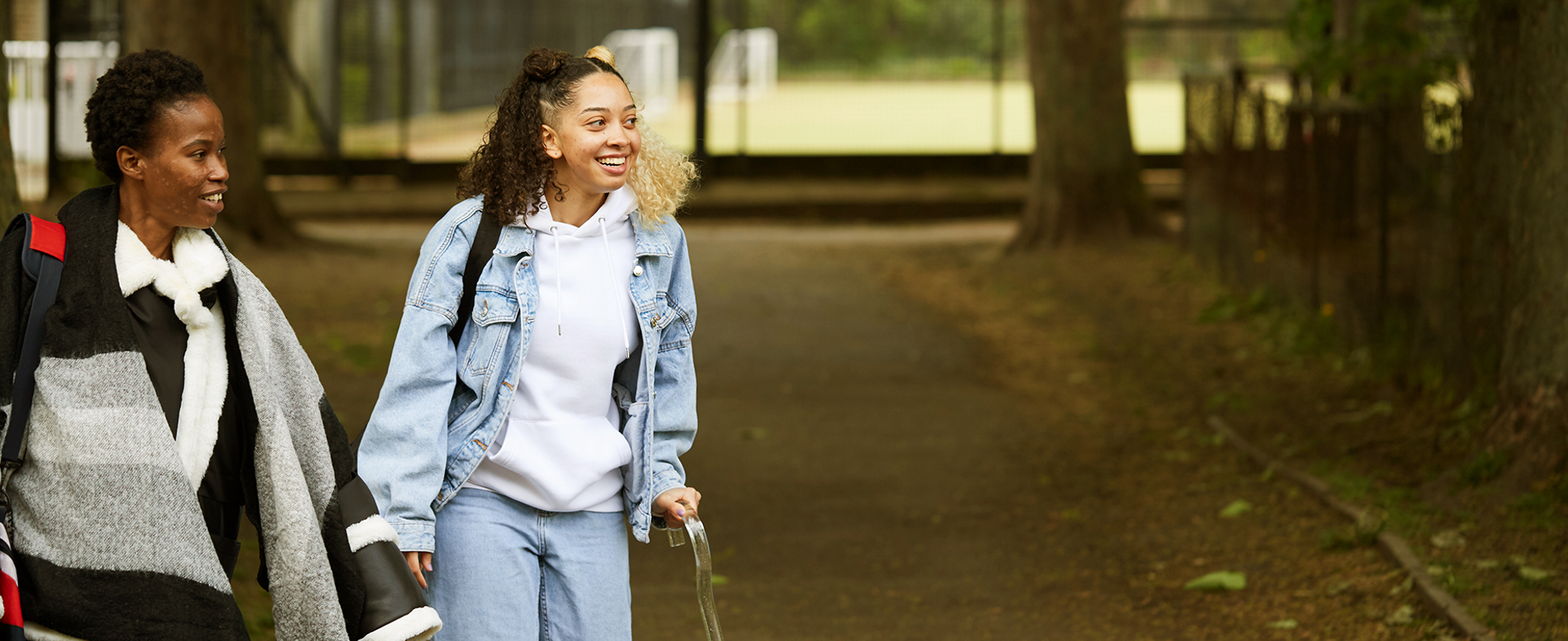 A girl with a crutch and an adult walking in the park.
