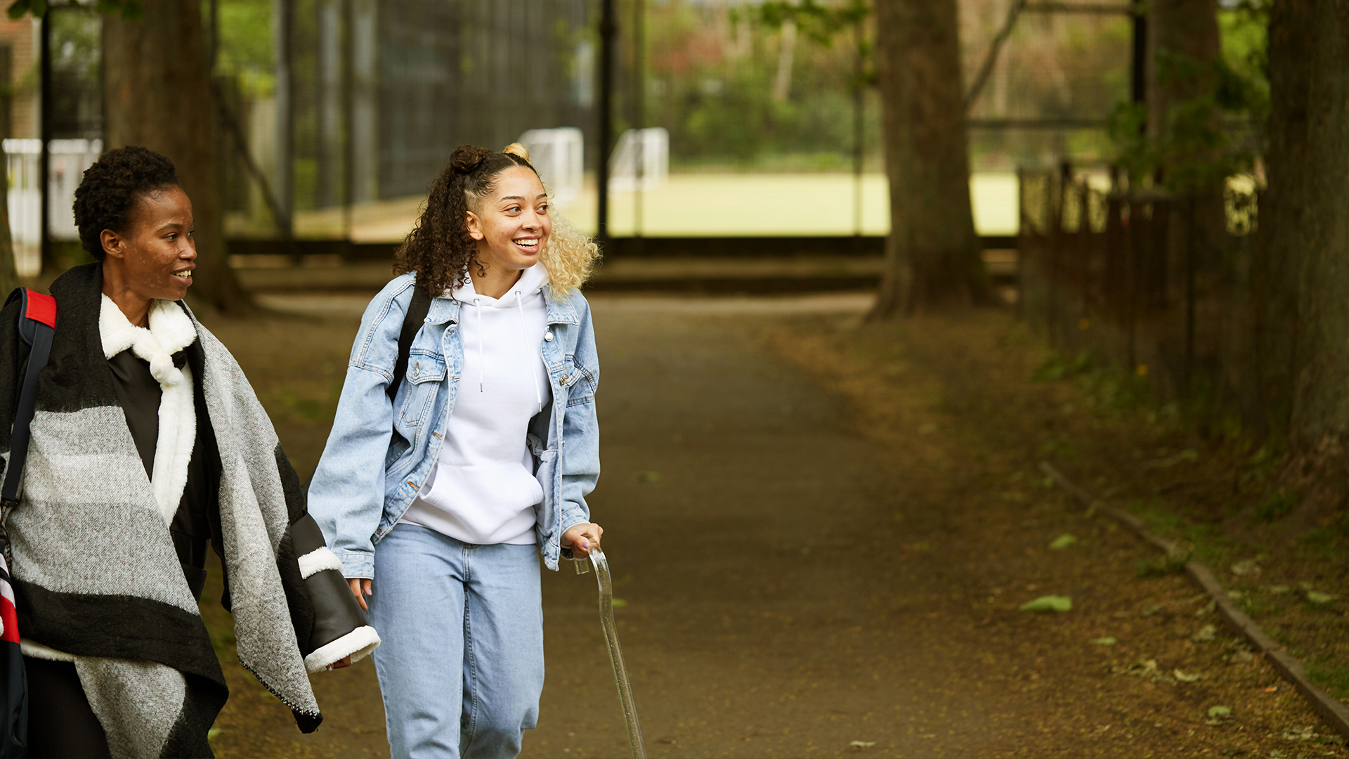 A girl with a crutch and an adult walking in the park.