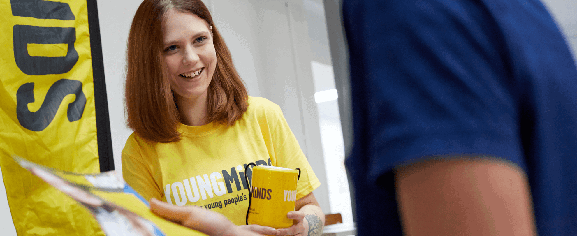 a YoungMinds volunteer wearing yellow YoungMinds shirt smiling in a fundraising event