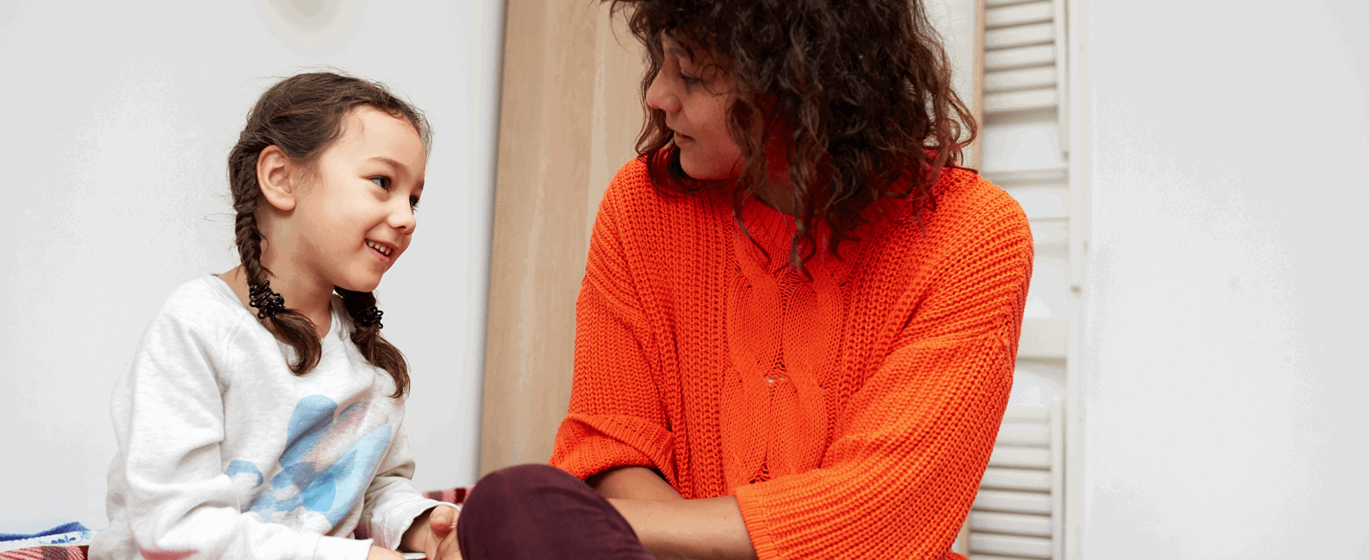 A mother and daughter sit and talk on the bed together