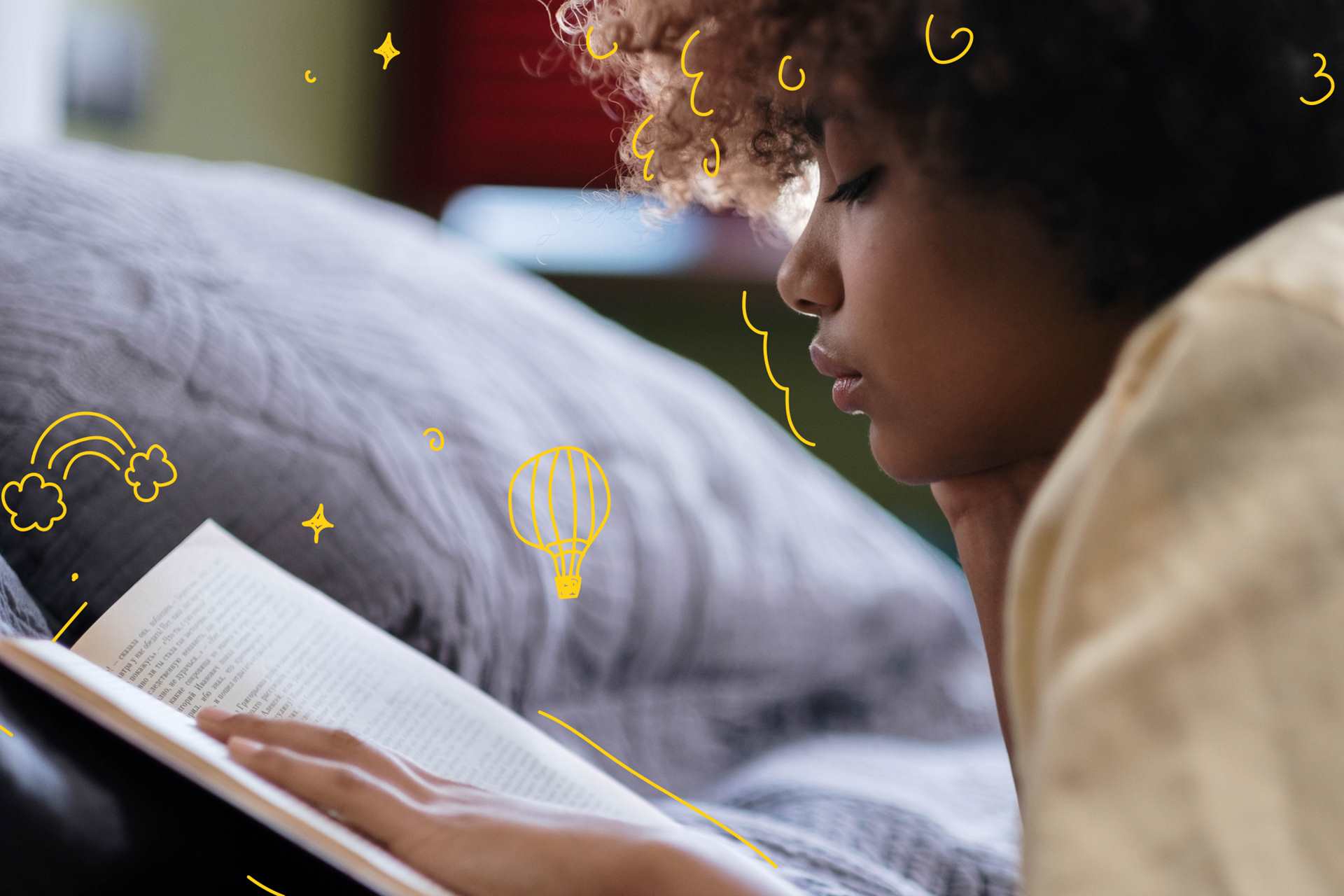 A young person reading a book lying on their front in bed.