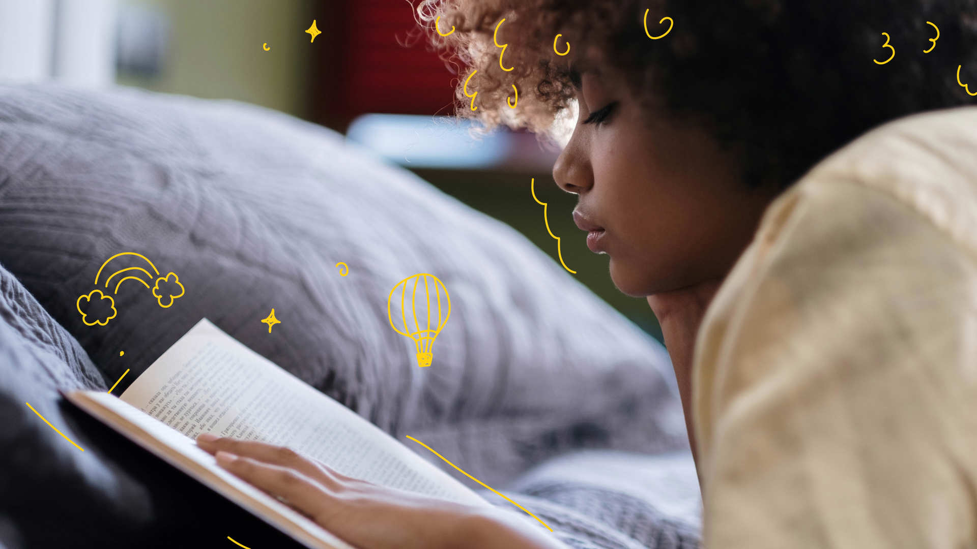 A young person reading a book lying on their front in bed.