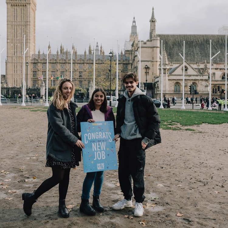 Three YoungMinds Activists standing in front of parliament holding a welcome card saying: 'Congrats on the new job'.