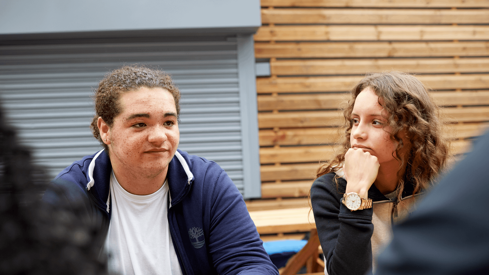 a girl with curly hair and a hand on her chin looking at a boy wearing blue jacket and a white shirt and  looks worried