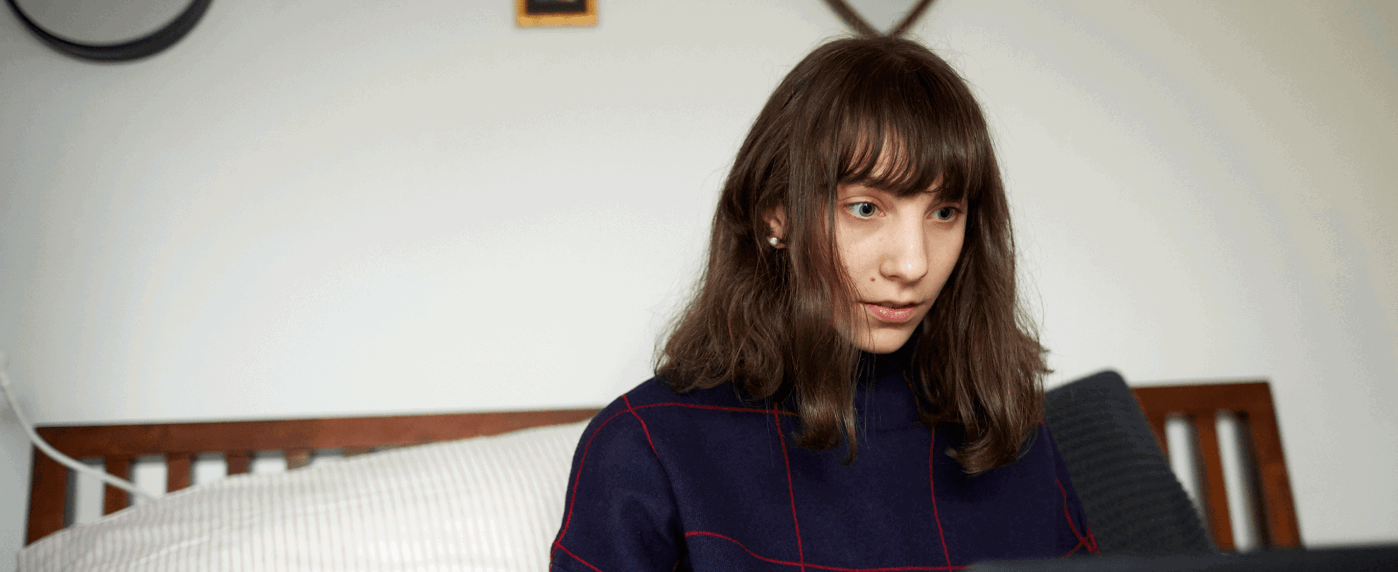 A girl sits on the end of her bed while looking at her laptop.