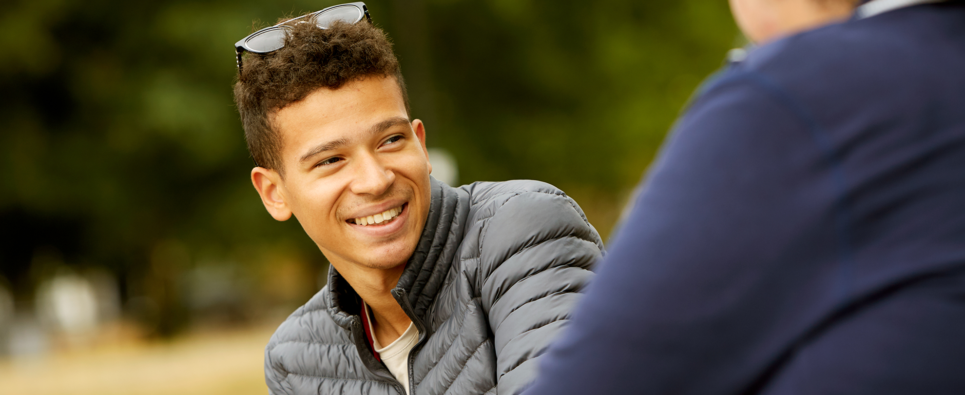 A boy smiling at his friend in the park.