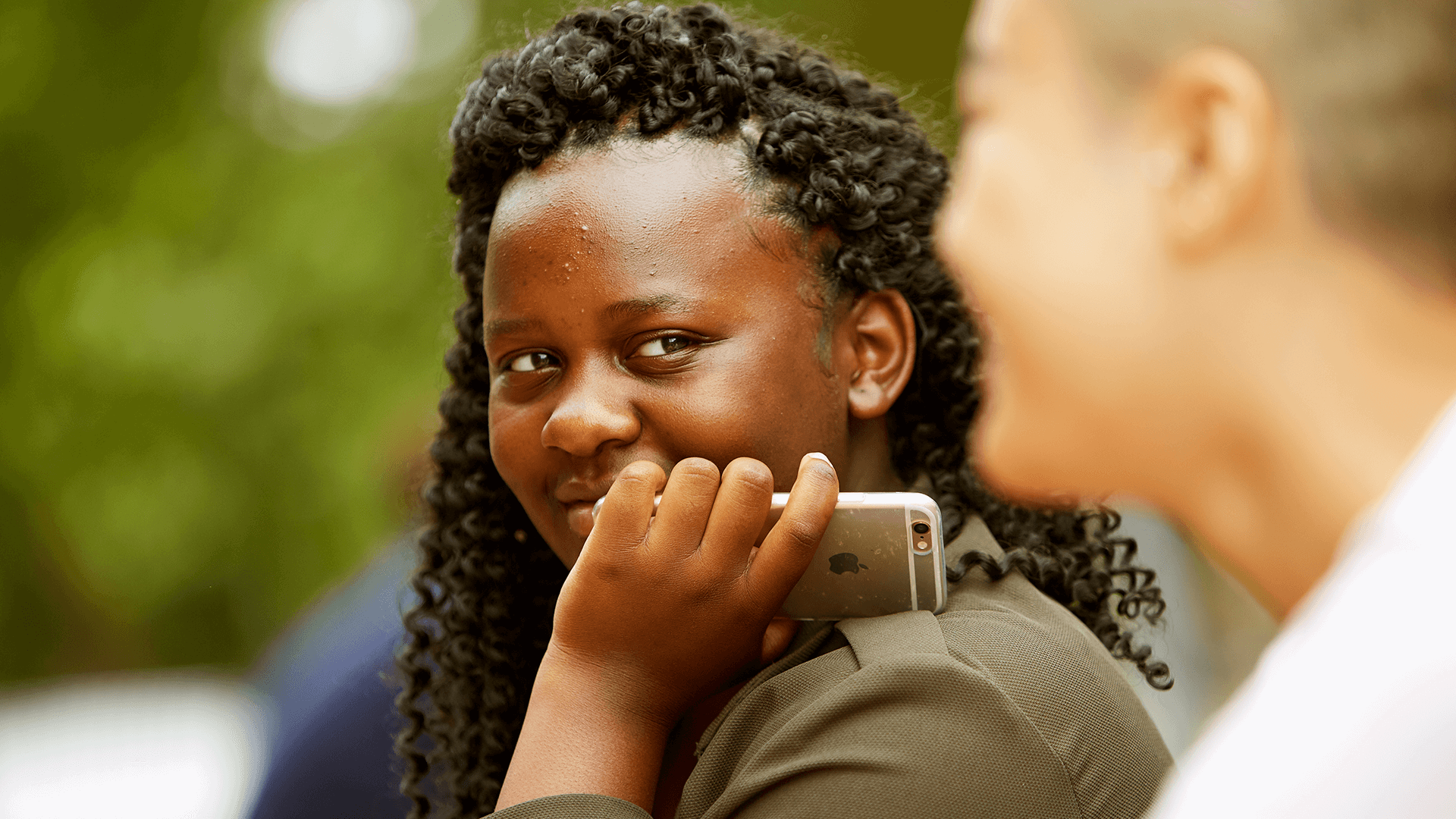 A young person smiling and holding their mobile against their cheek.