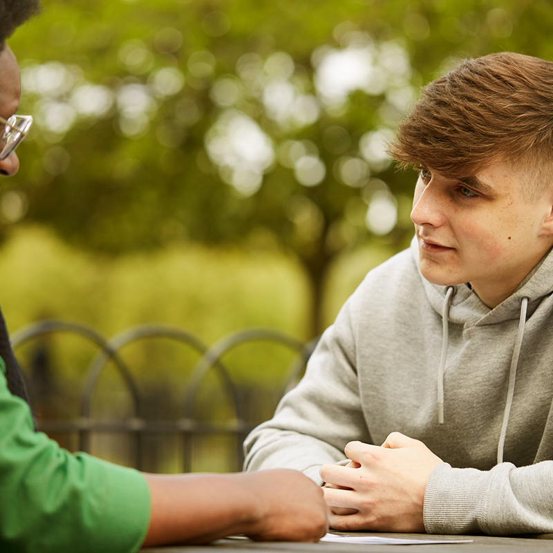 A young person talking to a trusted adult outside on a bench.