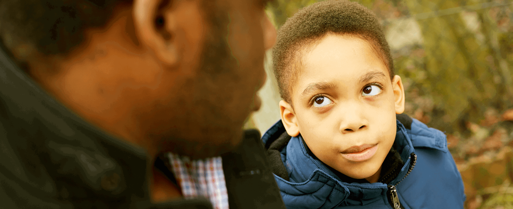 A child sat next to his father and looking up to him.