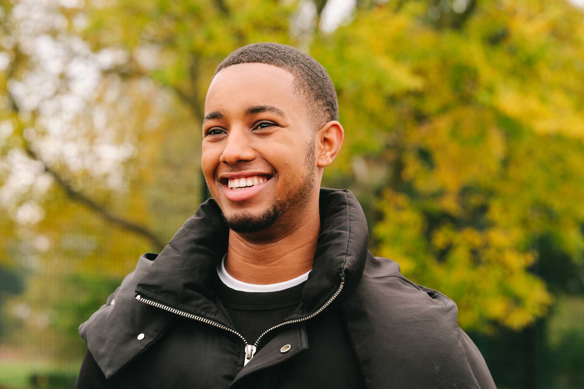 A young Black man smiling in the park.
