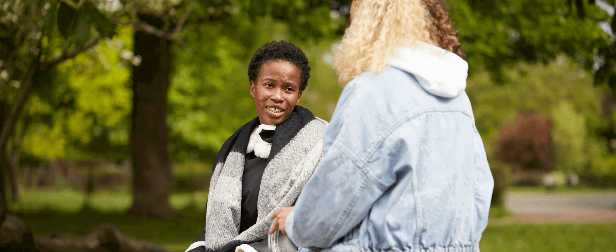 Two young people sitting together in a park and talking to each other.