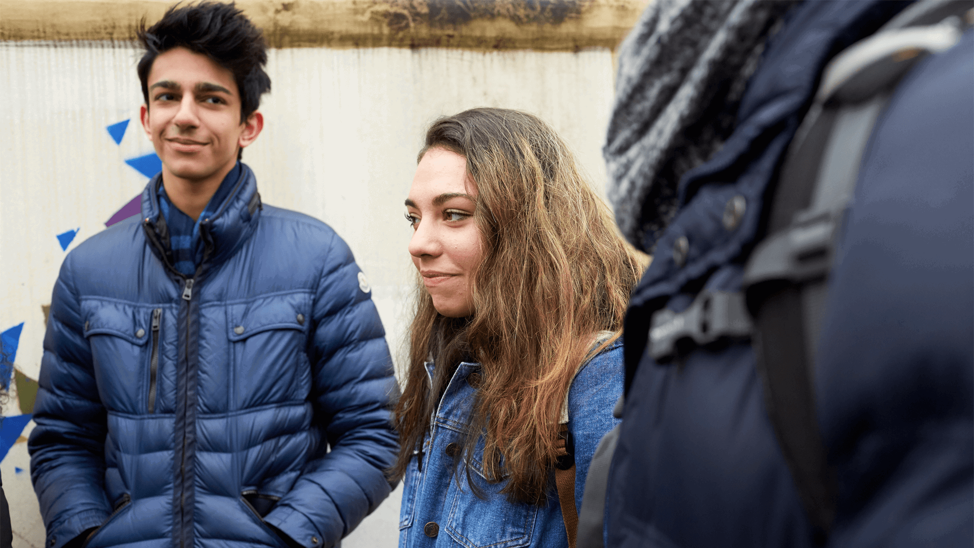 Three young people standing and talking in front of a graffiti wall.