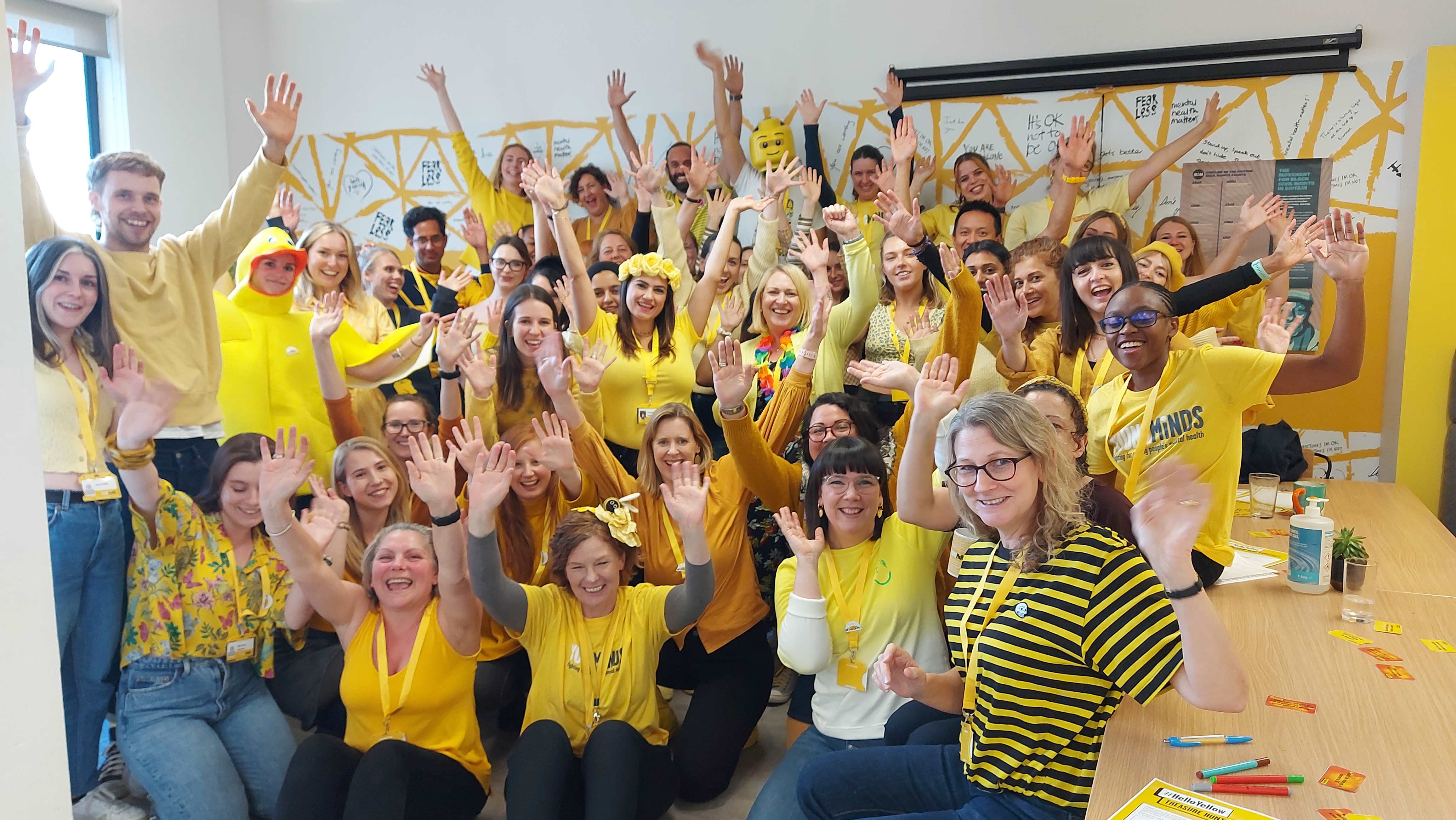 All the staff at YoungMinds wearing yellow and celebrating with their hands in the air on #HelloYellow and World Mental Health Day