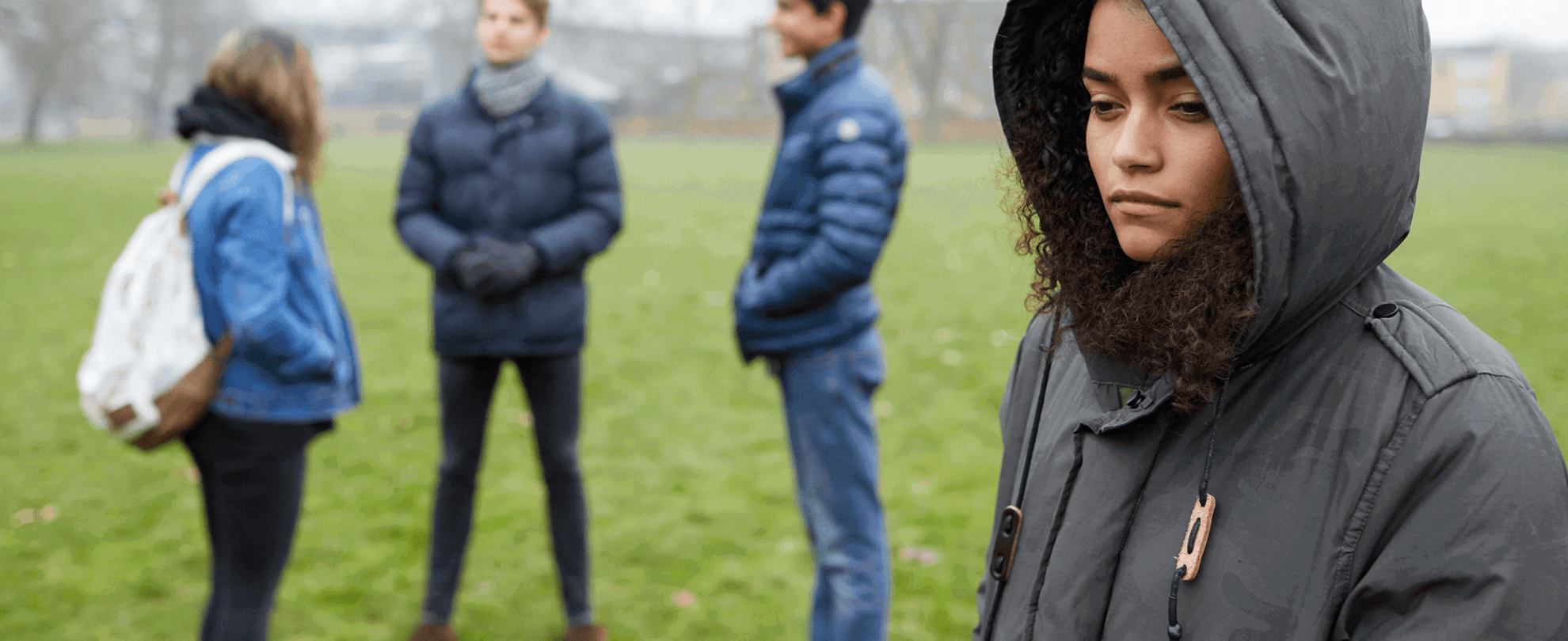 A young person stands alone feeling left out by three friends standing together.
