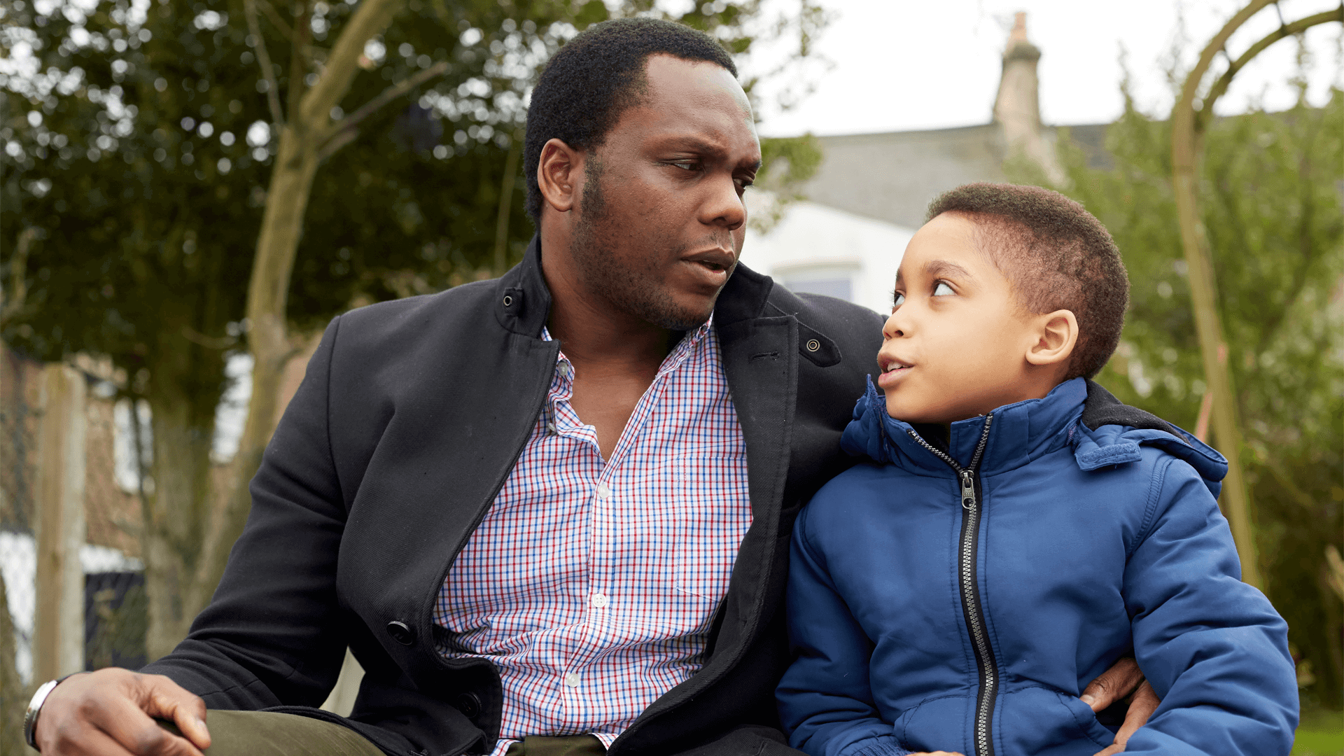 A father and son chatting outside near a fence 