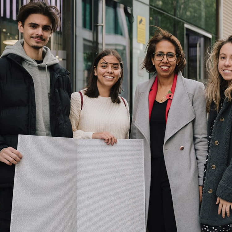 Three YoungMinds Activists with MP Munira Wilson holding the End The Wait card open on a page with all the signatures.