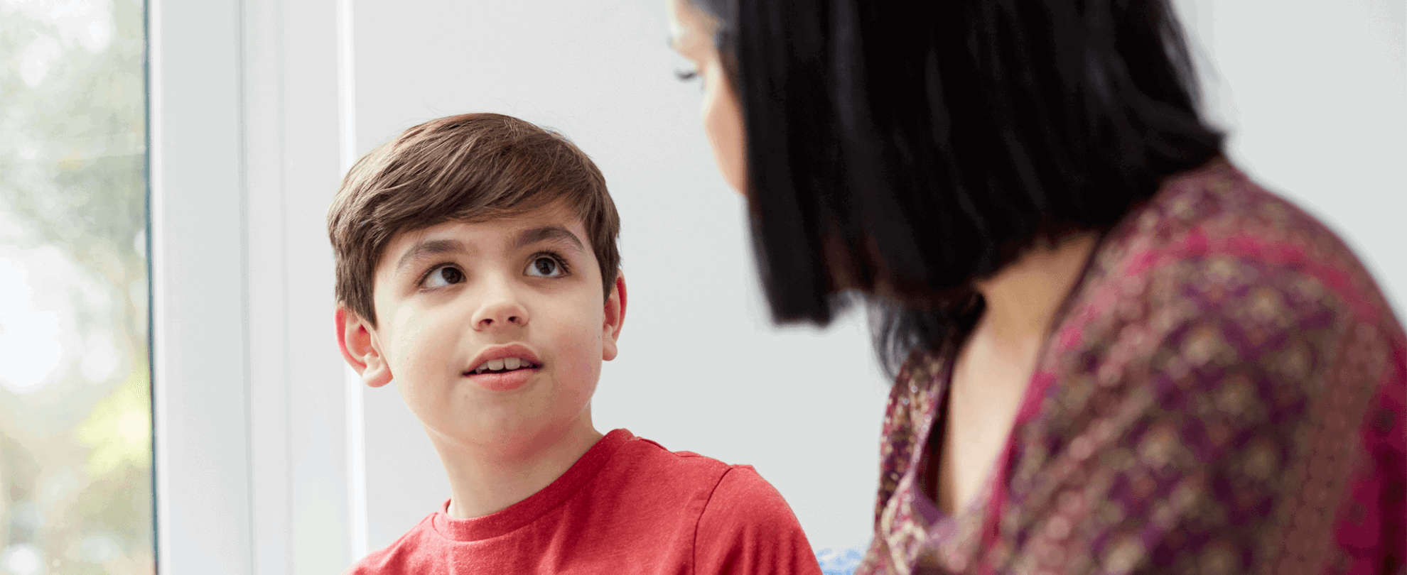A mother and her young son look at each other near a window