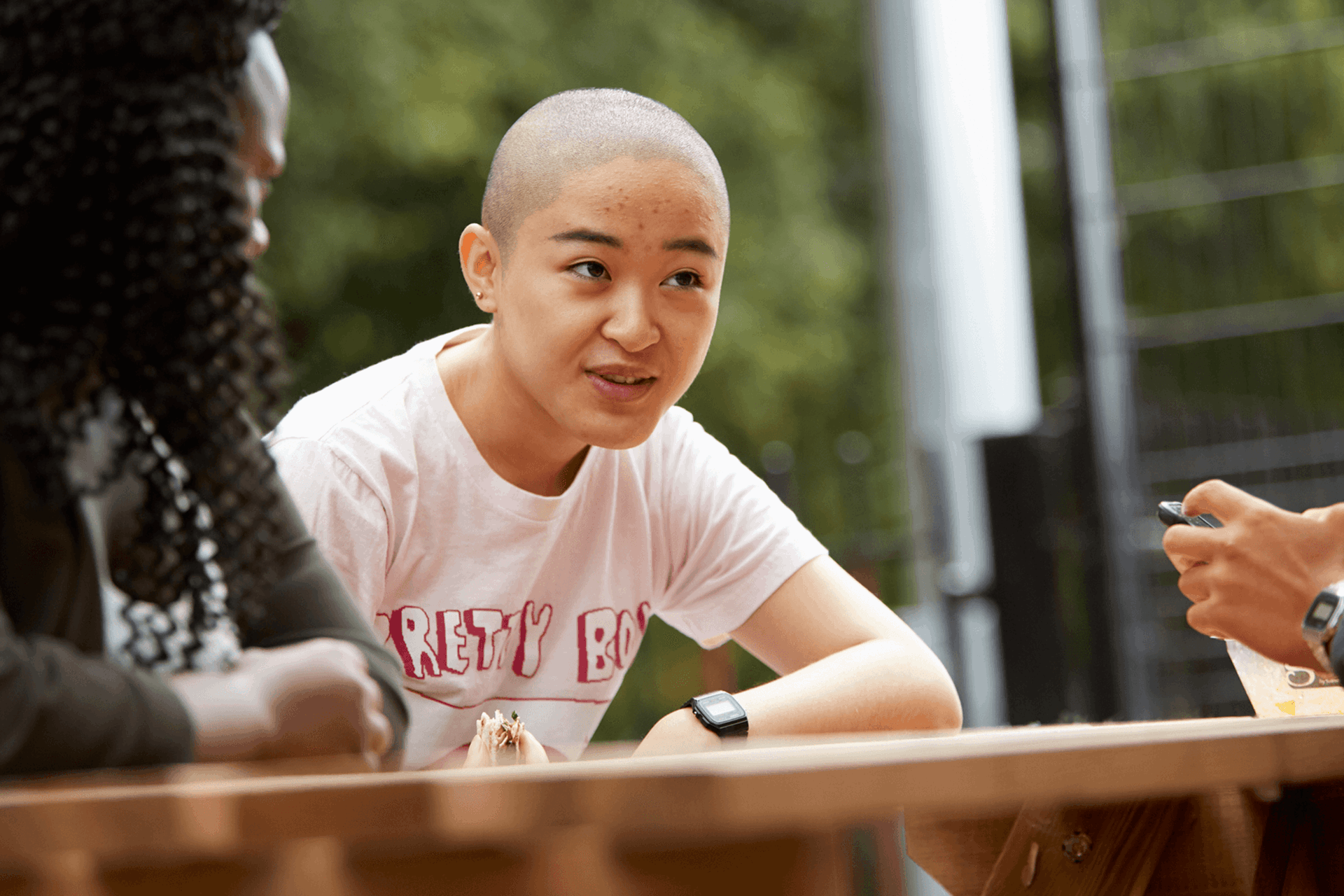 a-young-woman-with-shaved-head-talking-to-her-friends-while-sitting-on-a-dining-bench-in-a-park
