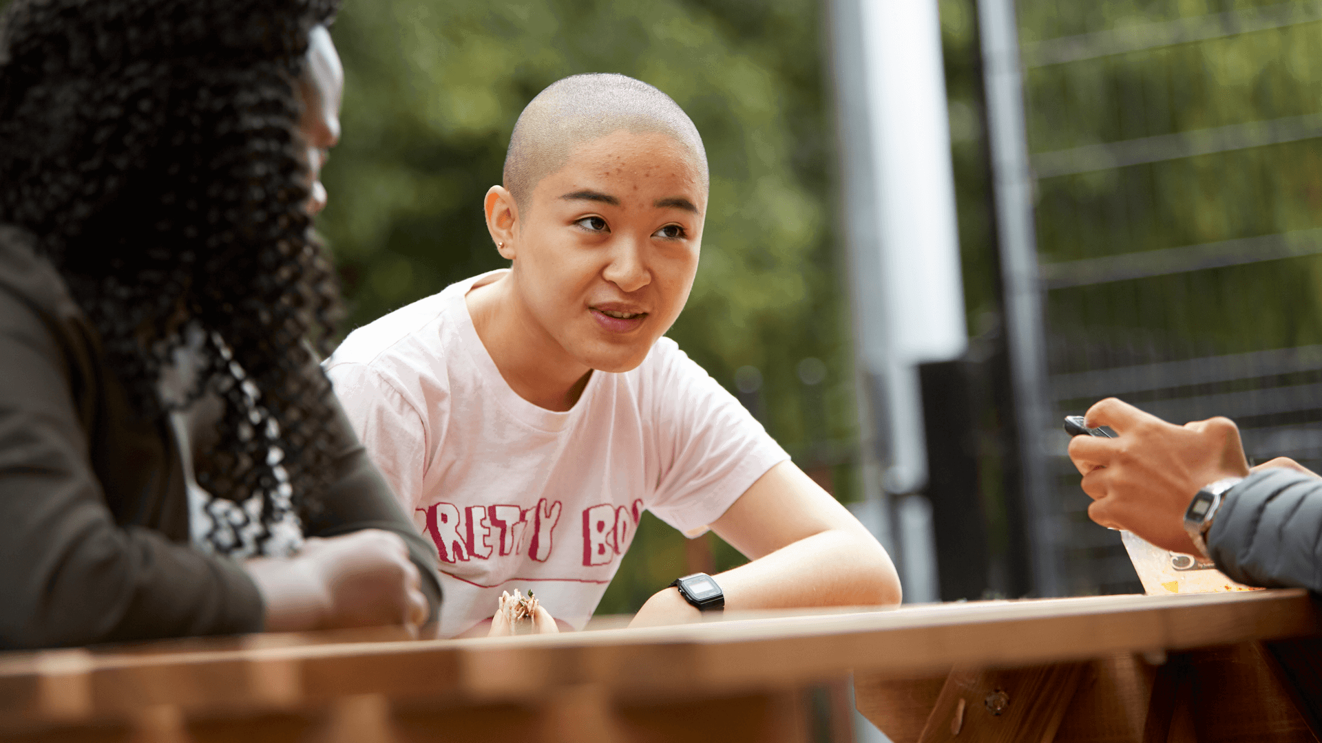 a-young-woman-with-shaved-head-talking-to-her-friends-while-sitting-on-a-dining-bench-in-a-park