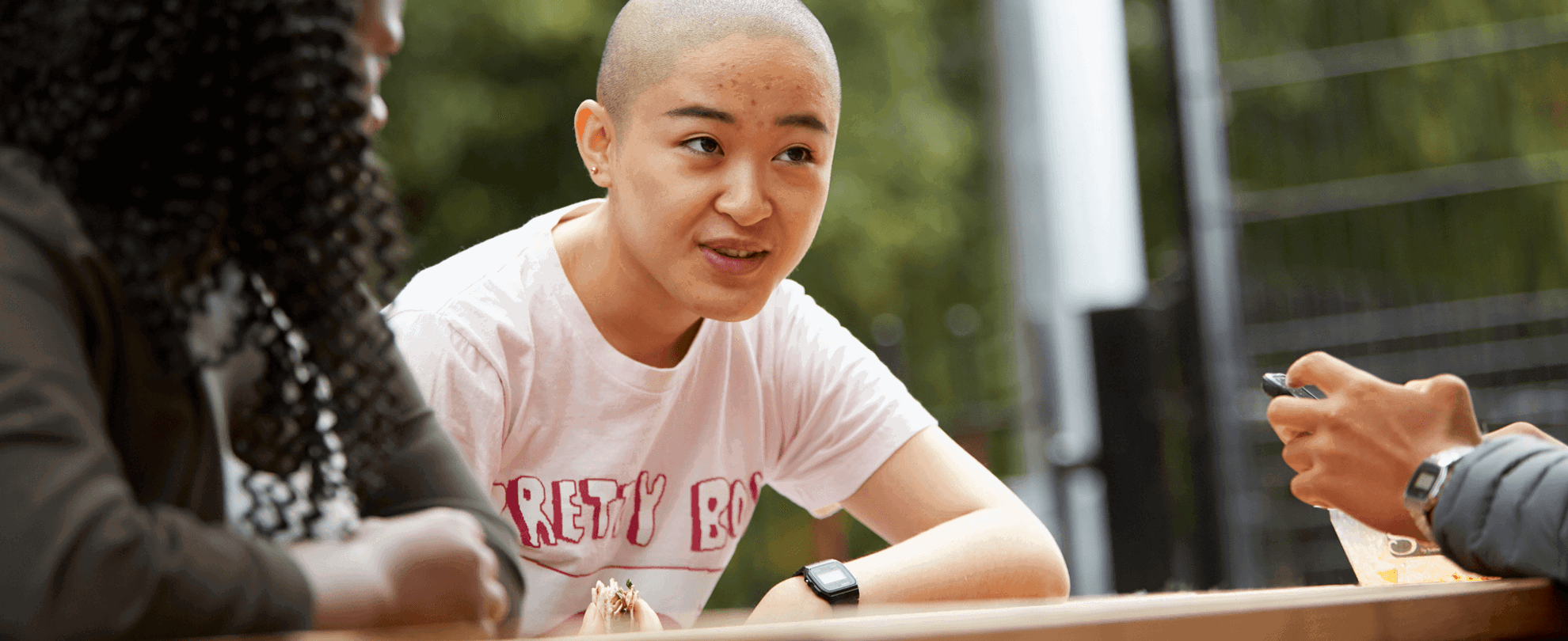 a-young-woman-with-shaved-head-talking-to-her-friends-while-sitting-on-a-dining-bench-in-a-park