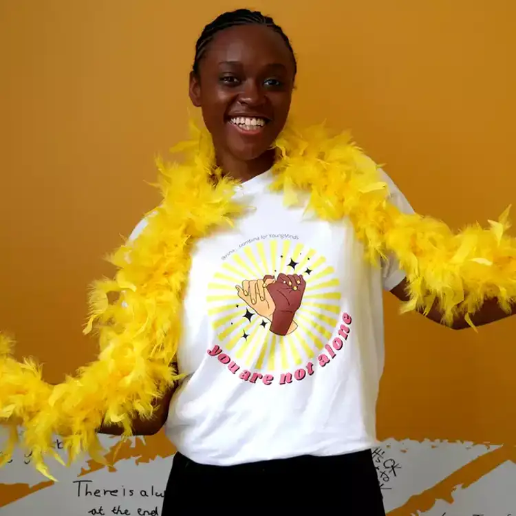 A woman smiling wearing a yellow feather bower and Nina Bombina bespoke 'You are not alone' graphic Hello Yellow T-shirt